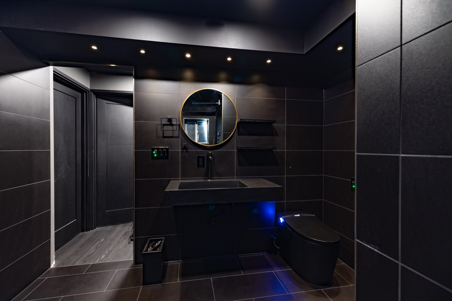 Charcoal tiled bathroom with a floating sink and round gold-rimmed mirror