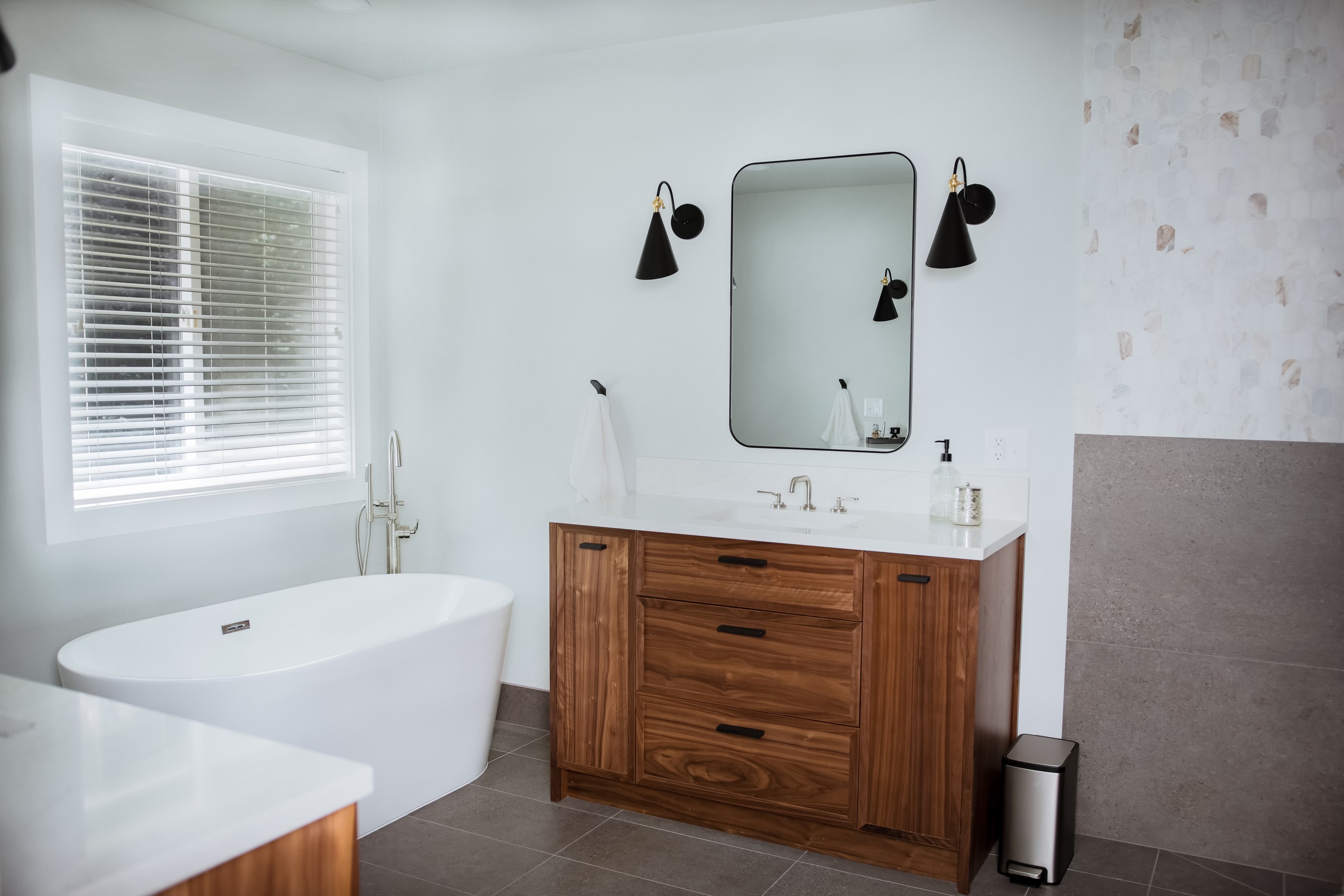 A bright bathroom with a natural wood vanity and freestanding tub