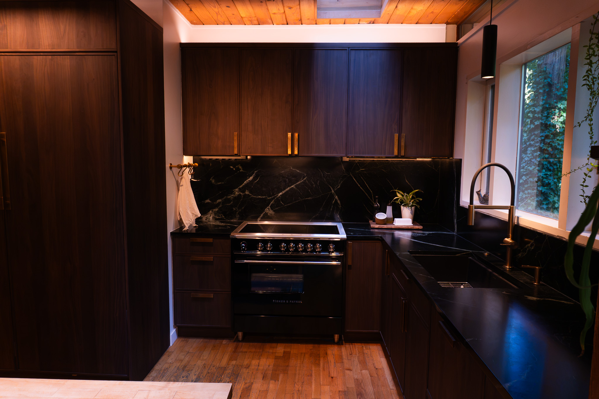 A completed kitchen with rich wood cabinetry, dark veined surfaces, and warm brass fittings